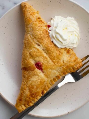 A raspberry turnover on a plate with whipped cream and a fork.