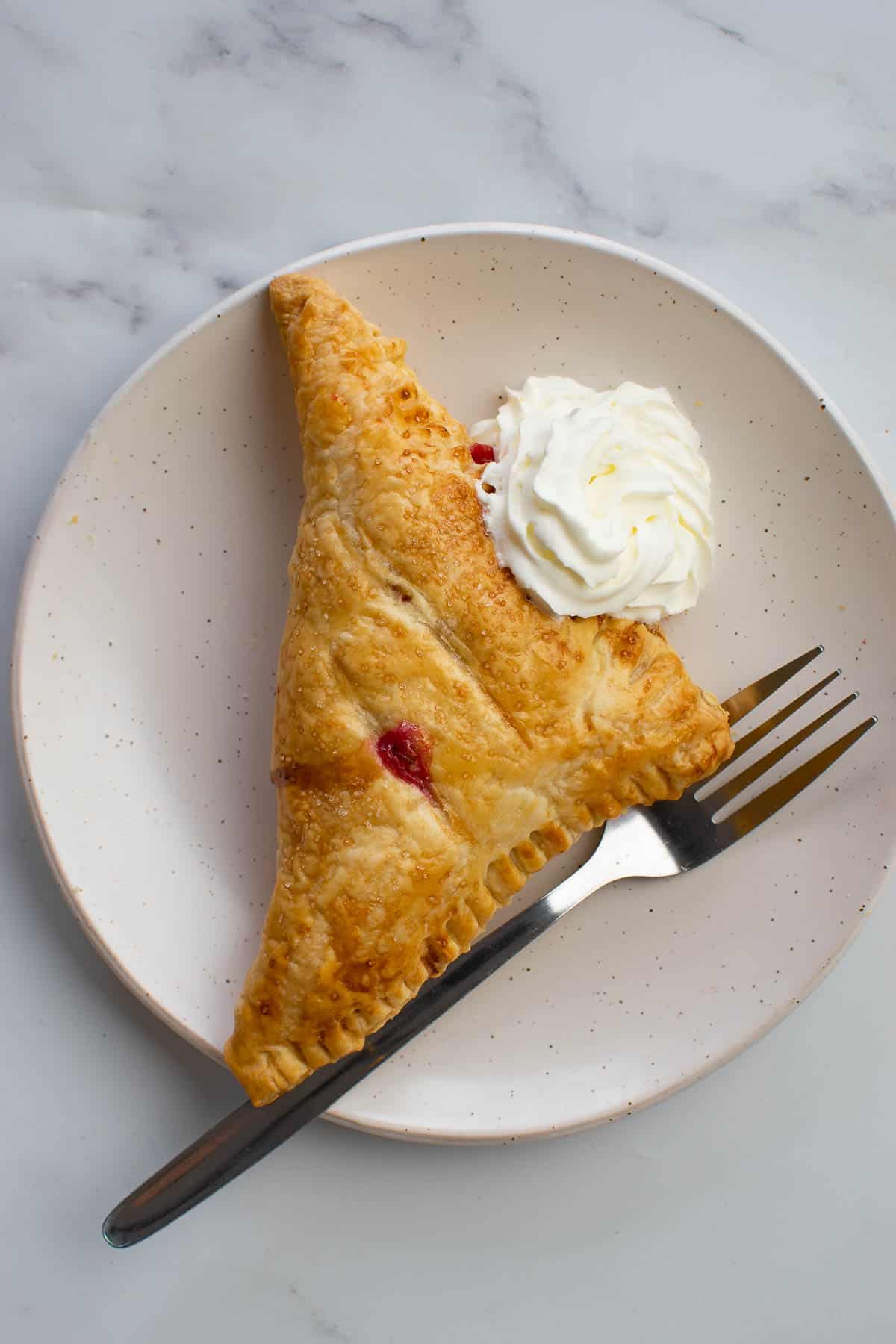 A raspberry turnover with cream on a plate.