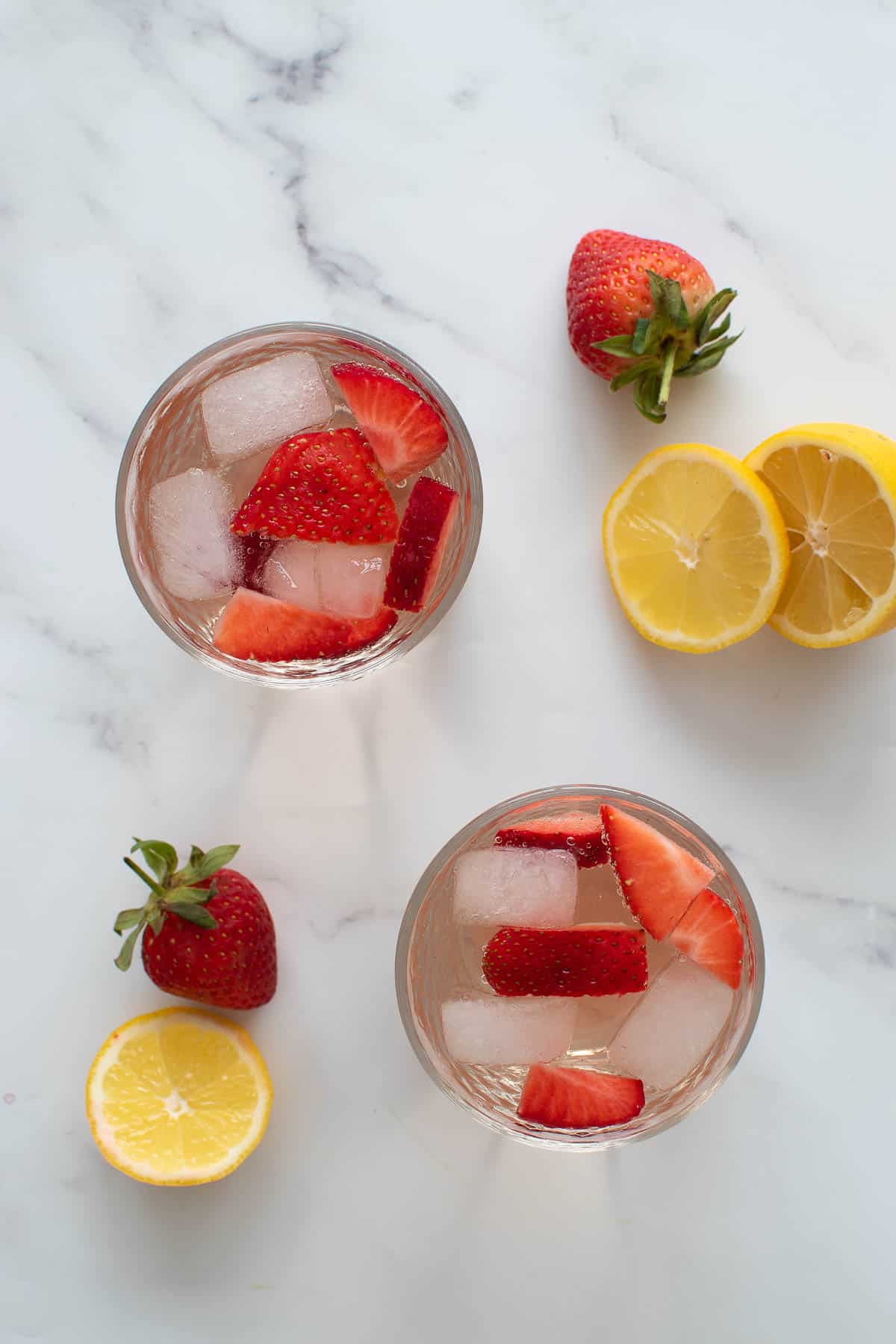 Two glasses of rose wine spritzer with strawberries and lemon.