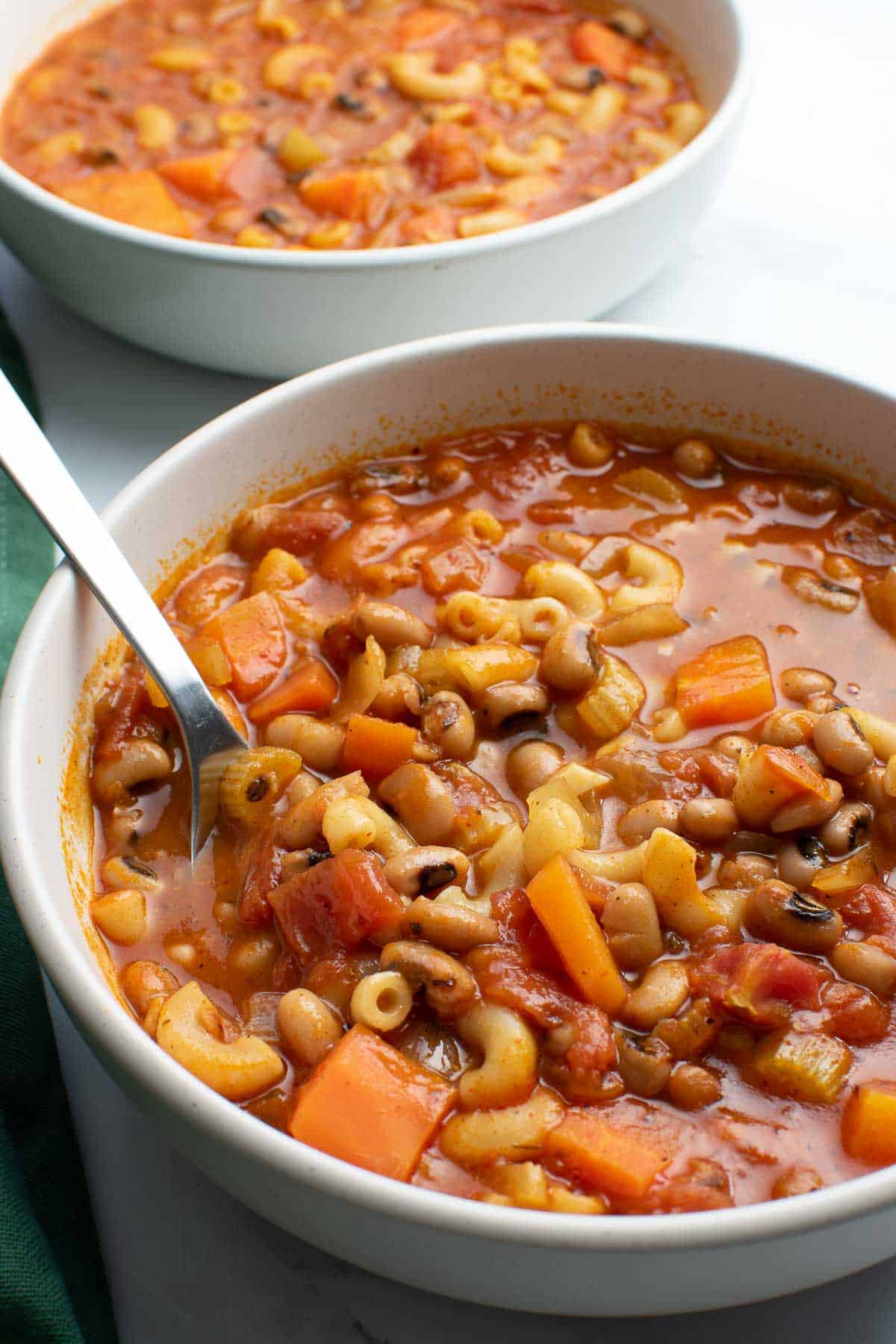 Tomato and black eyed pea soup with a spoon lifting up the ingredients.