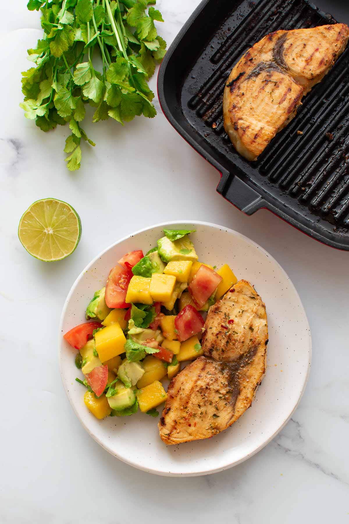 Baked swordfish on a plate with mango avocado salad.