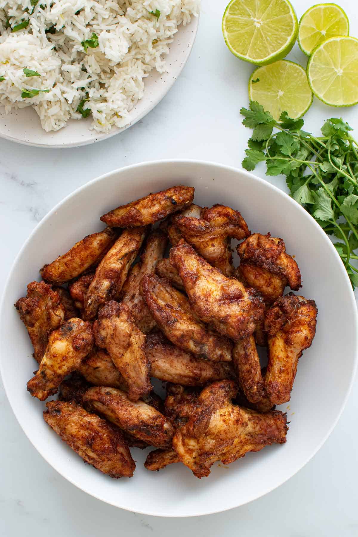 A bowl of Cajun chicken wings, with rice, lime and cilantro on the side.