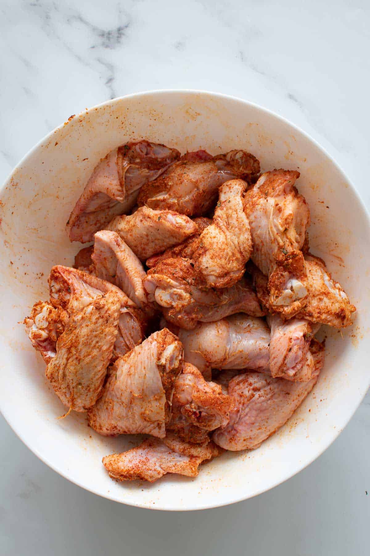 Seasoned raw chicken wings in a mixing bowl.