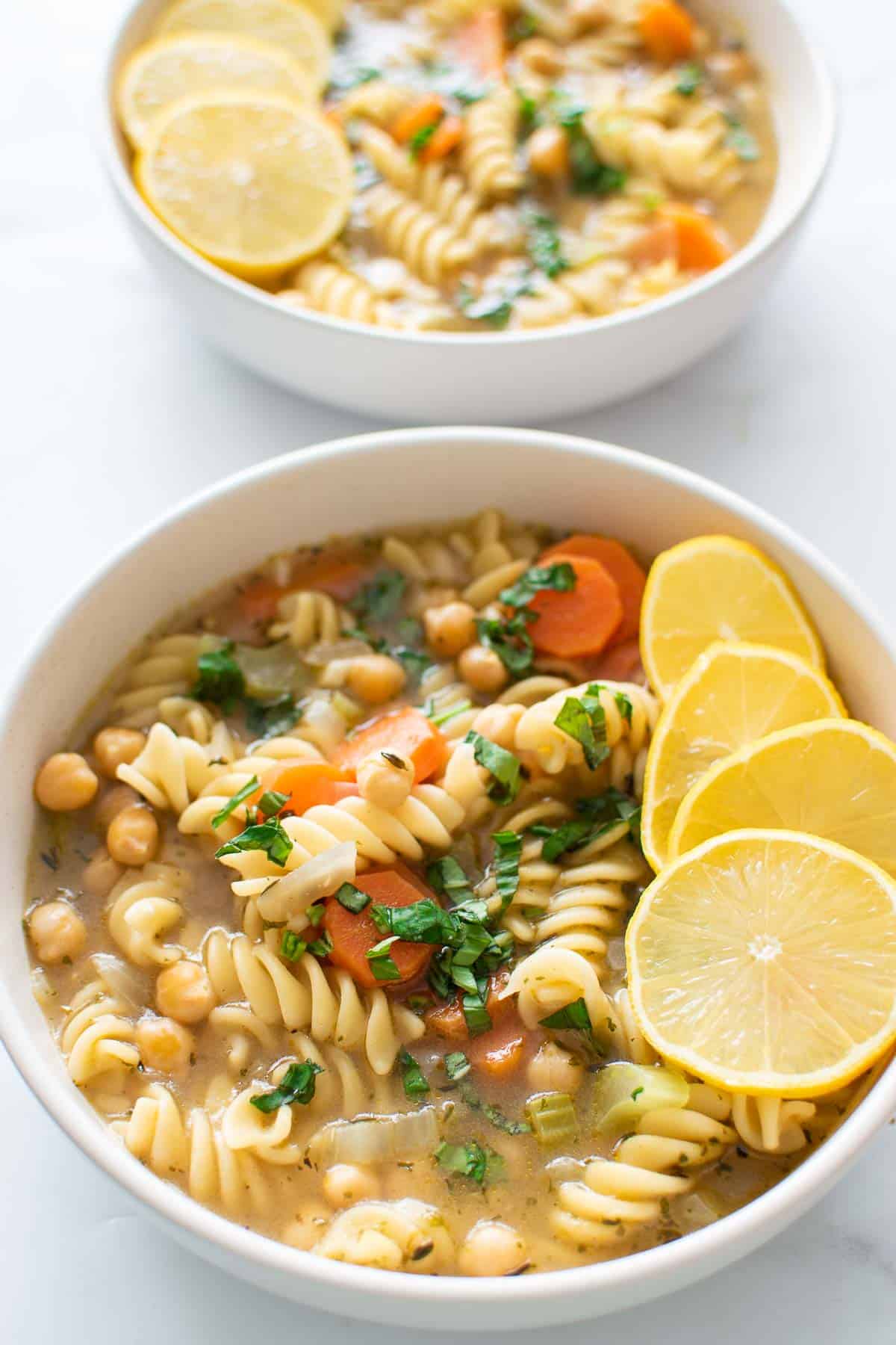 Two bowls of vegetarian soup with chickpeas, noodles and carrots.