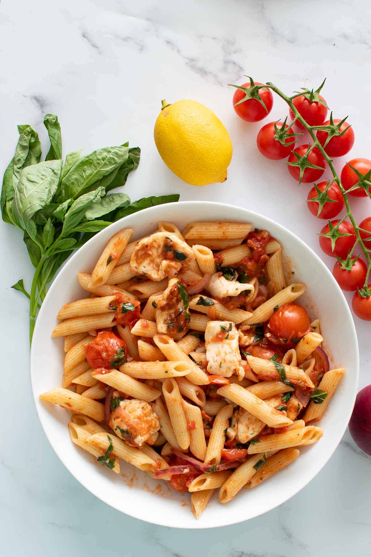 Halloumi pasta, basil, lemon and cherry tomatoes on a table.