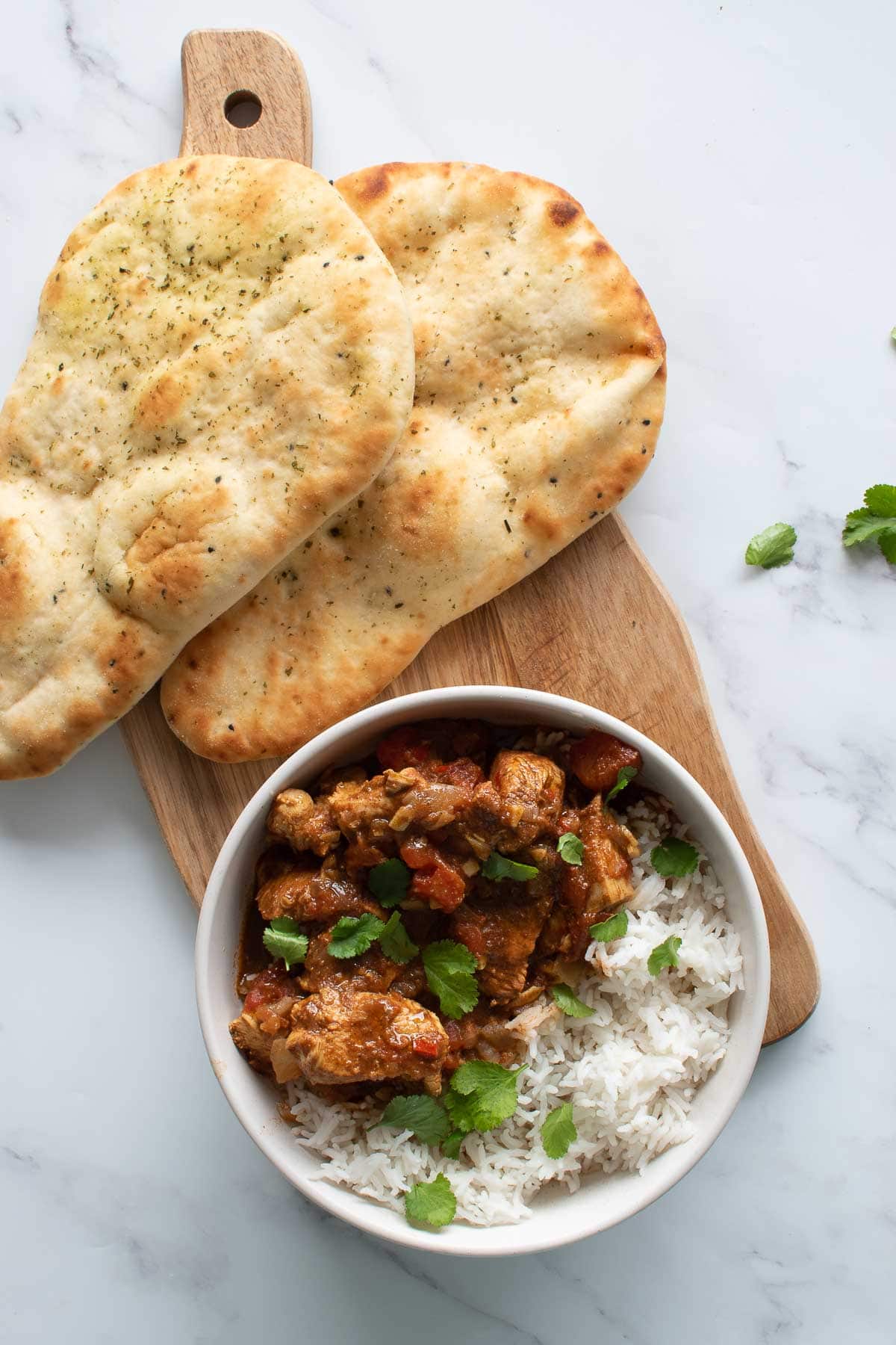 A bowl of chicken curry with naan on the side.