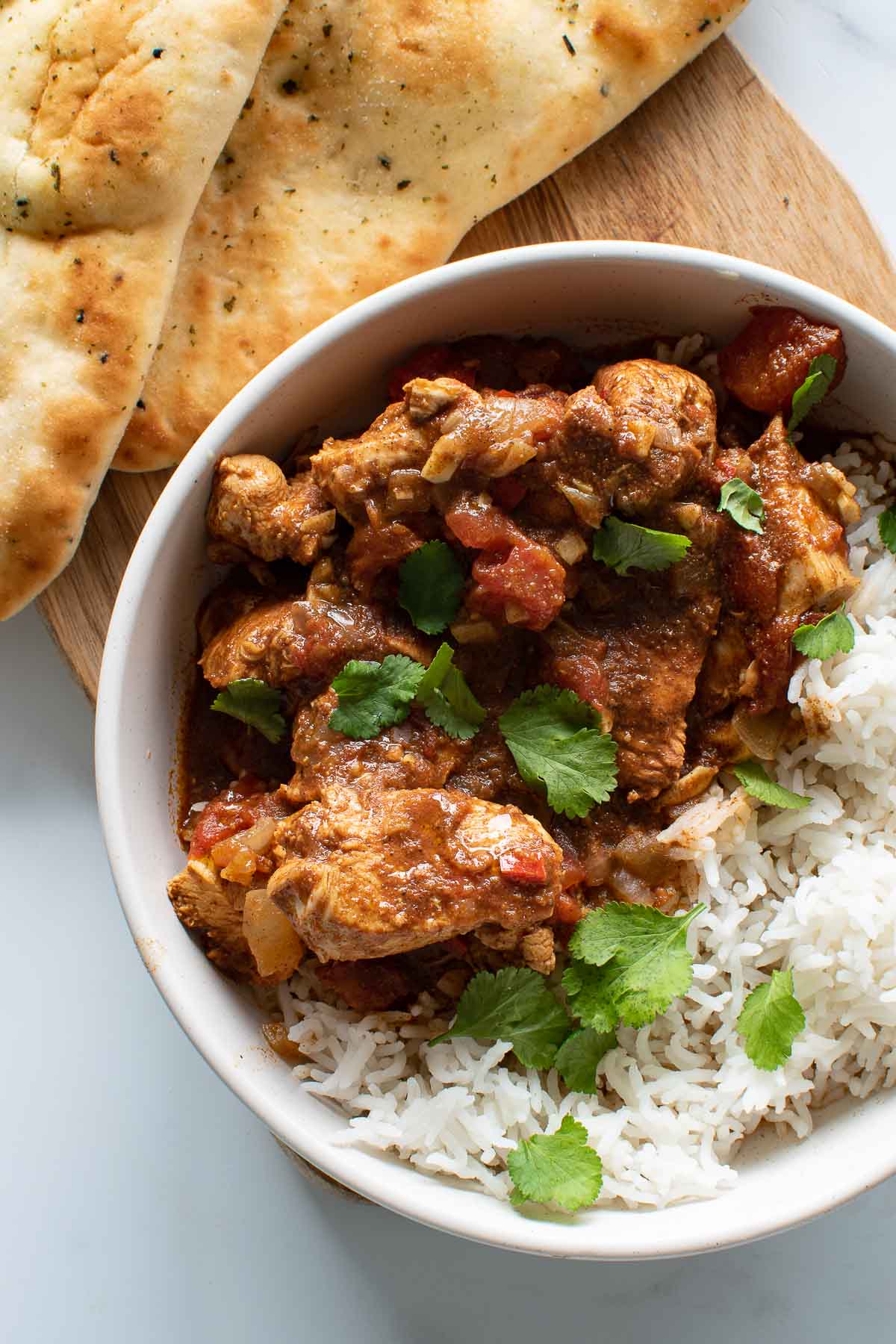 Chicken curry and rice in a bowl, with naan in the background.