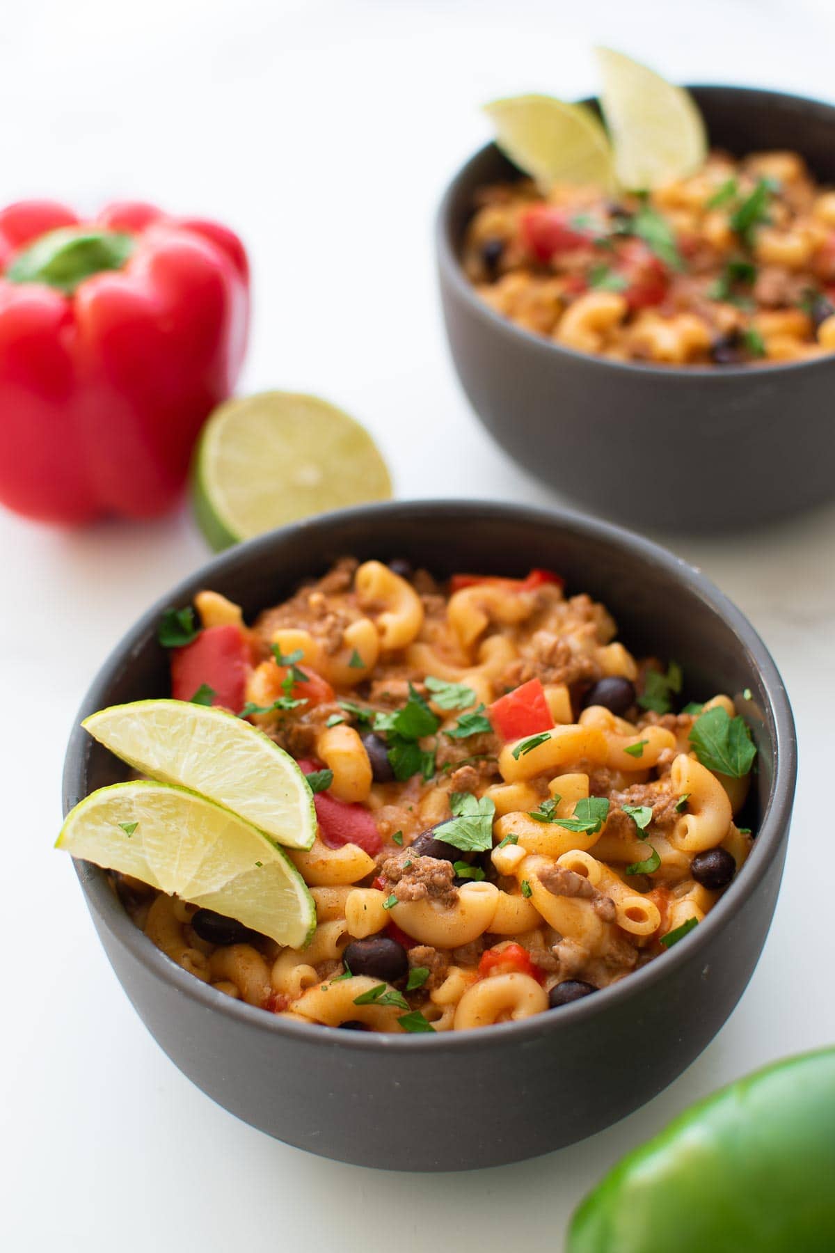 Bowl of cheesy chili mac with lime wedges on the side.
