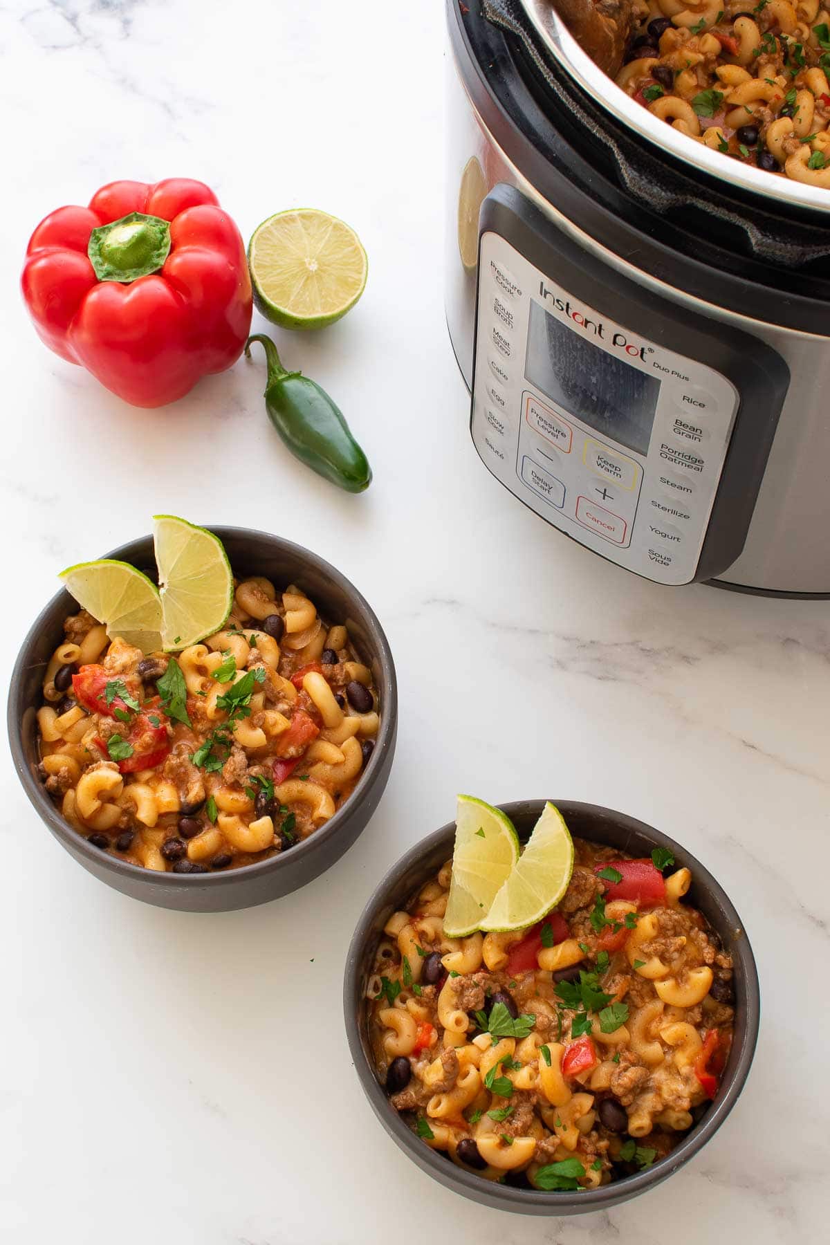 Two bowls of chili mac, with vegetables on the side and a pressure cooker in the background.