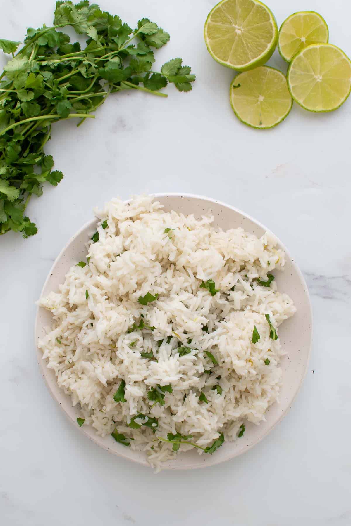 A plate of cilantro lime rice with lime slices and cilantro on the side.