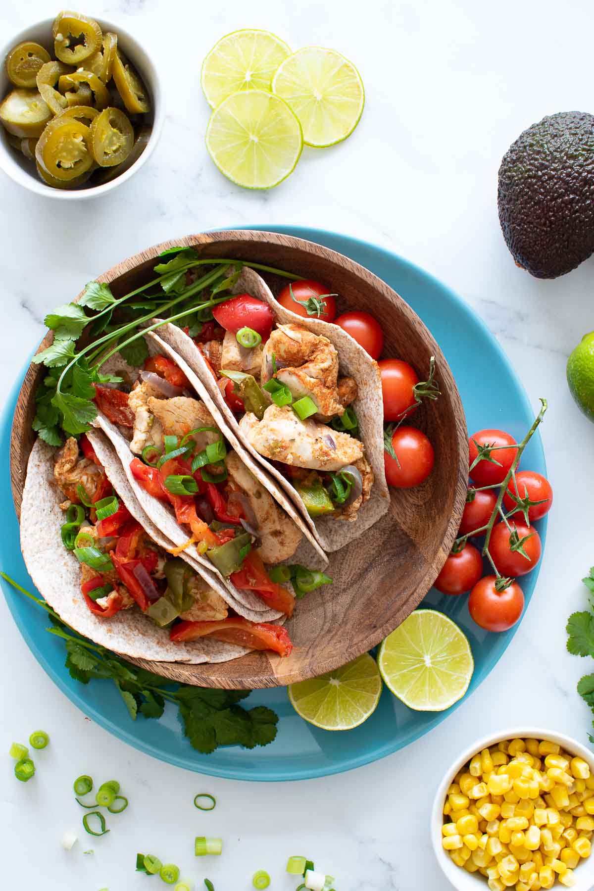 A table with a plate of Instant Pot fajitas, with garnishes and side dishes scattered around.