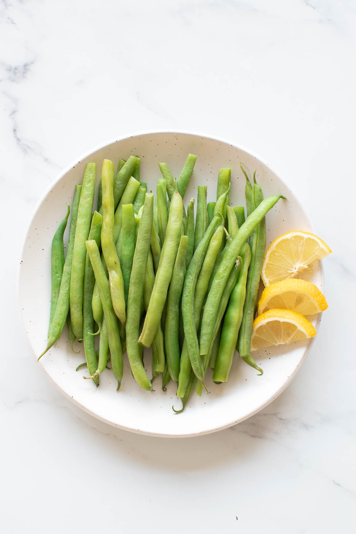 A plate of steamed green beans with lemon wedges.