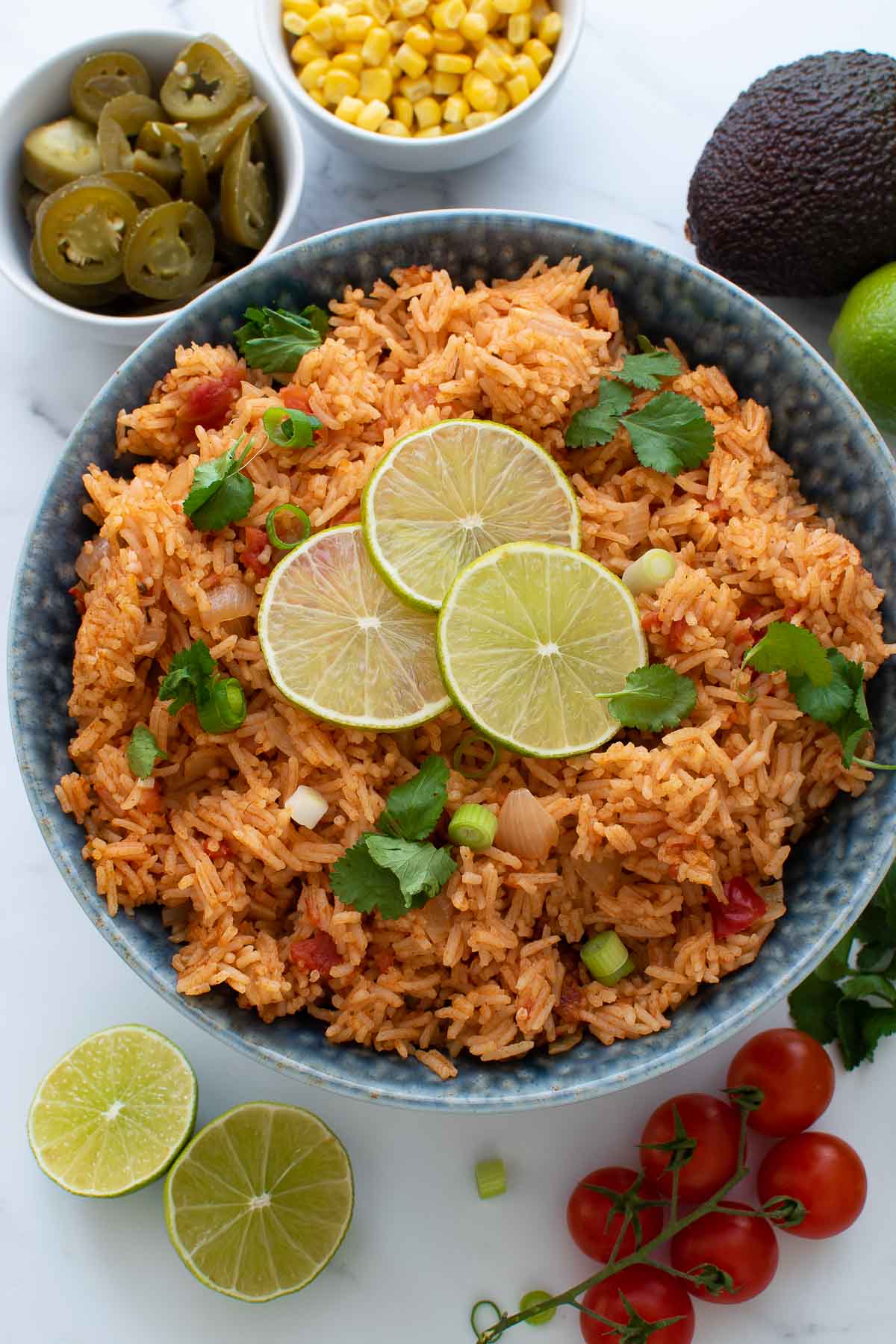 Mexican rice in a bowl, surrounded by sides and garnishes.