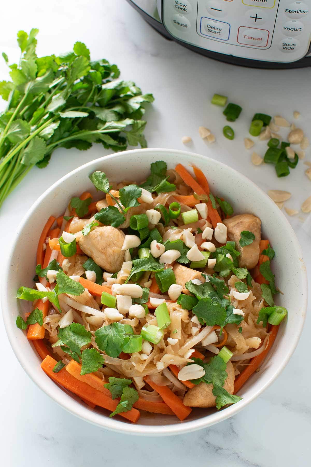 Pressure cooked pad thai on a table with garnishes in the background.