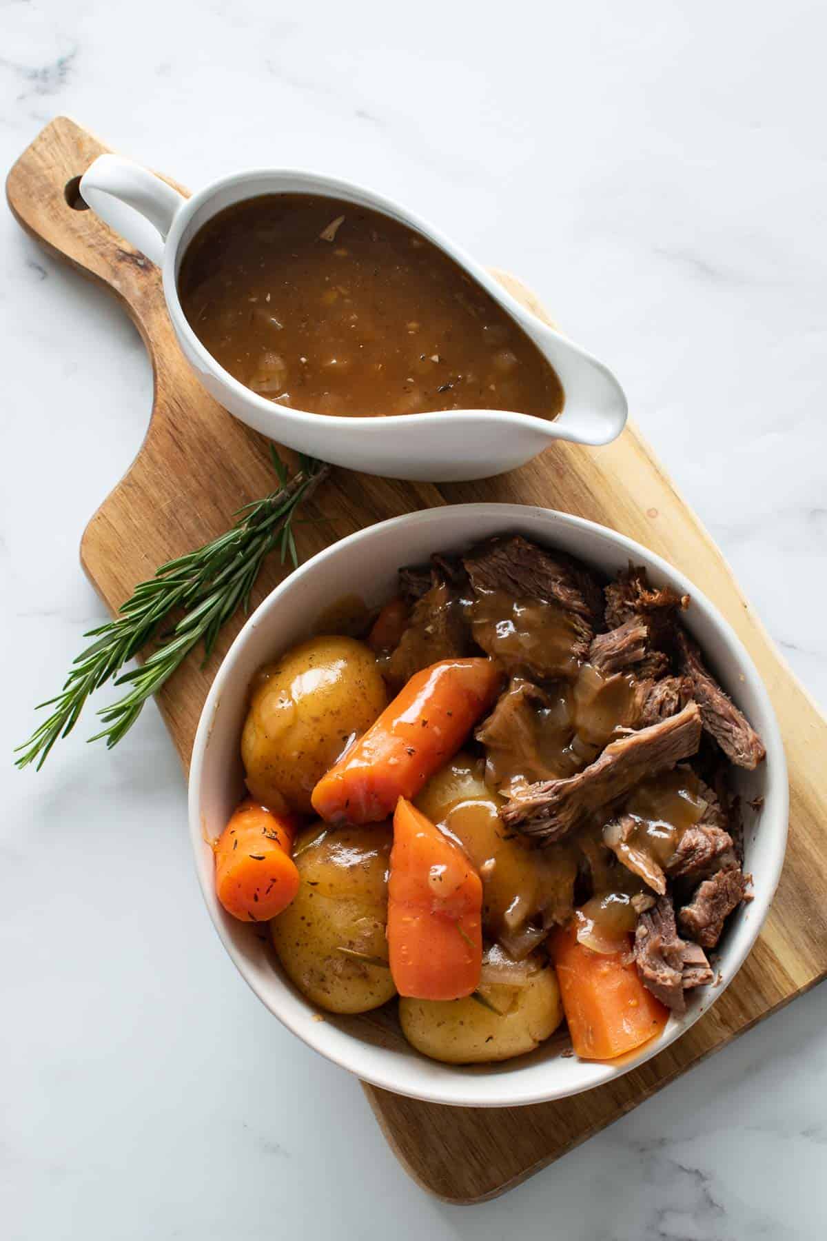 Pressure cooked pot roast and gravy on a wooden board.