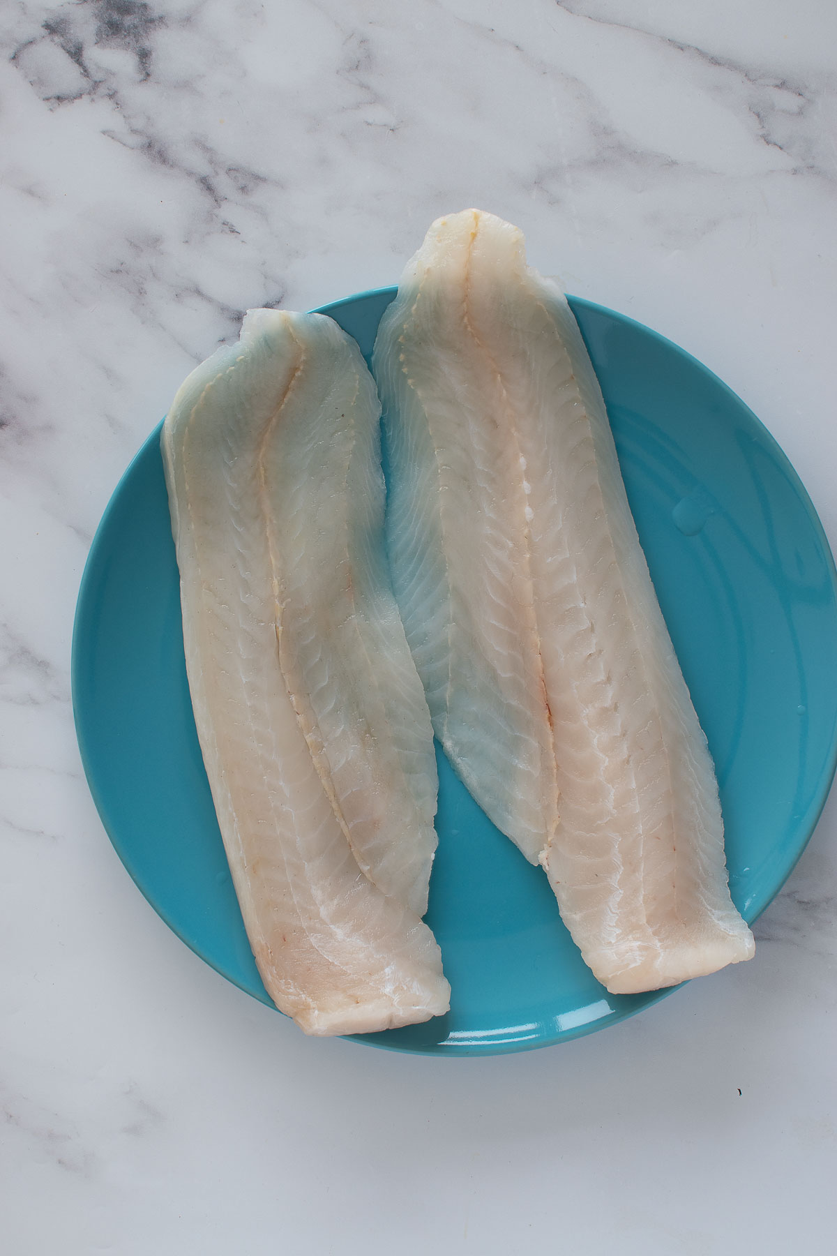 Two hake fish fillets on a plate.