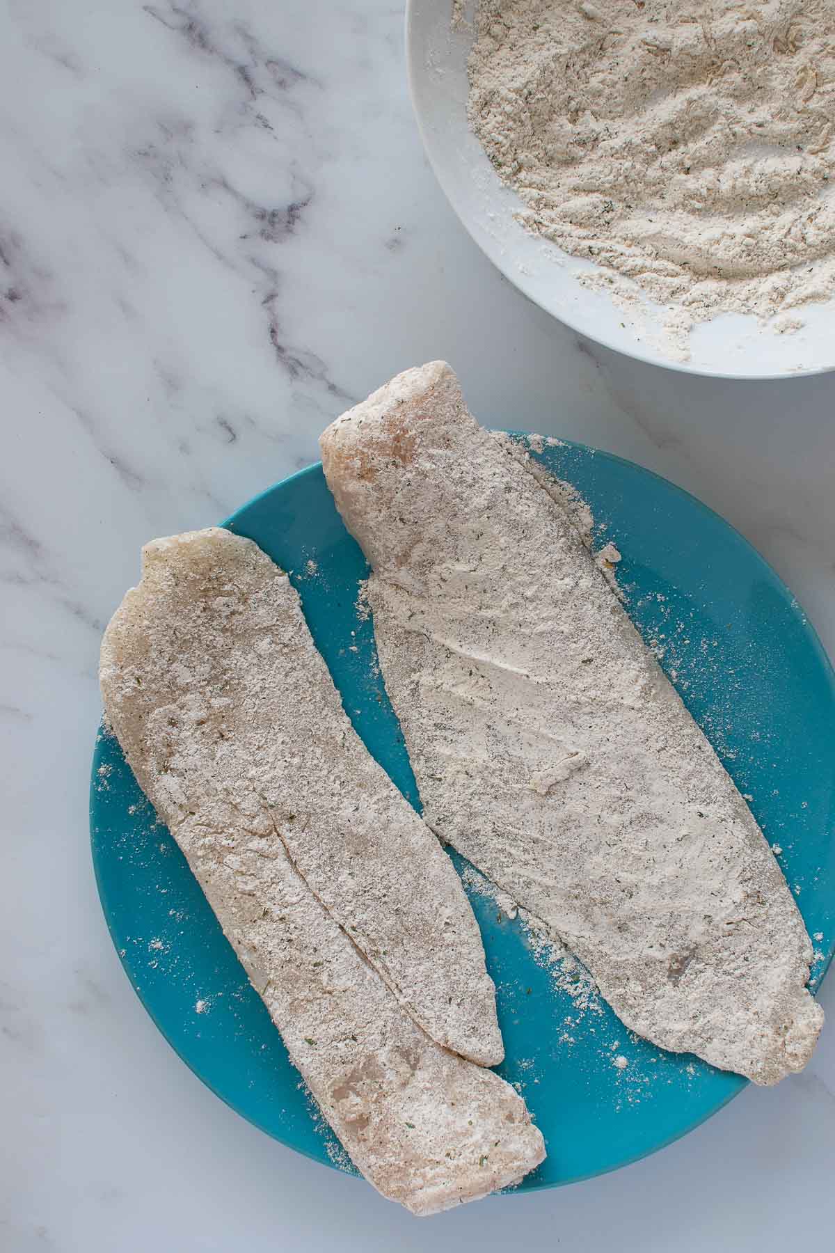 Hake fillets coated in flour and seasoning.