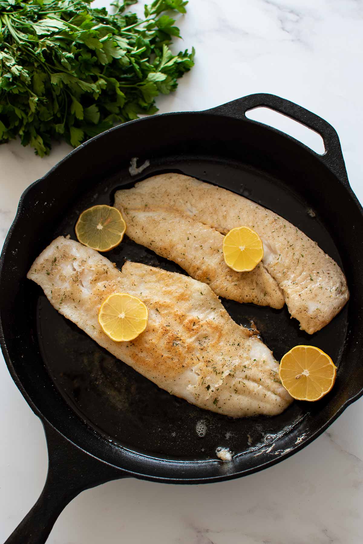 Pan fried hake with lemon slices in a cast iron pan.