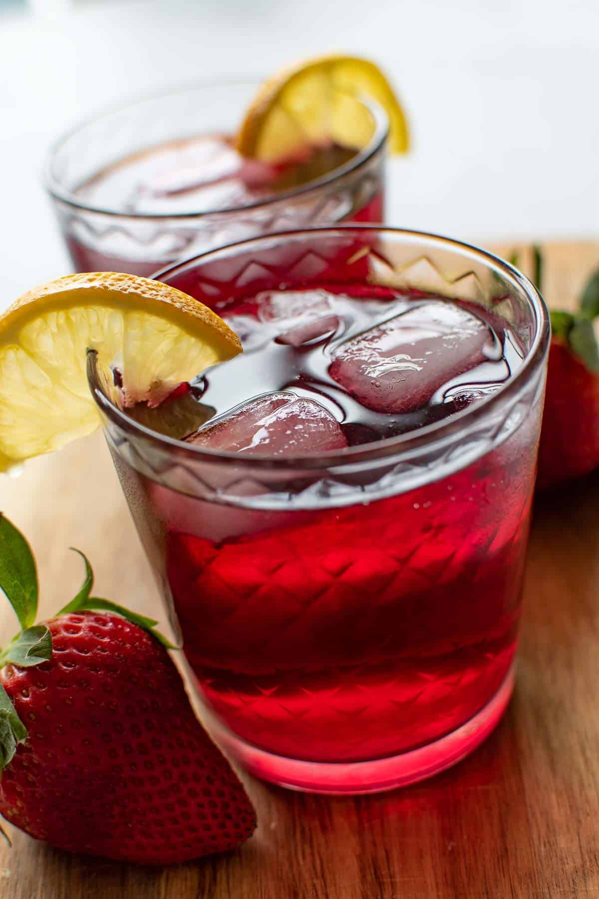 Red wine spritzer in a glass with a lemon wedge and ice cubes.