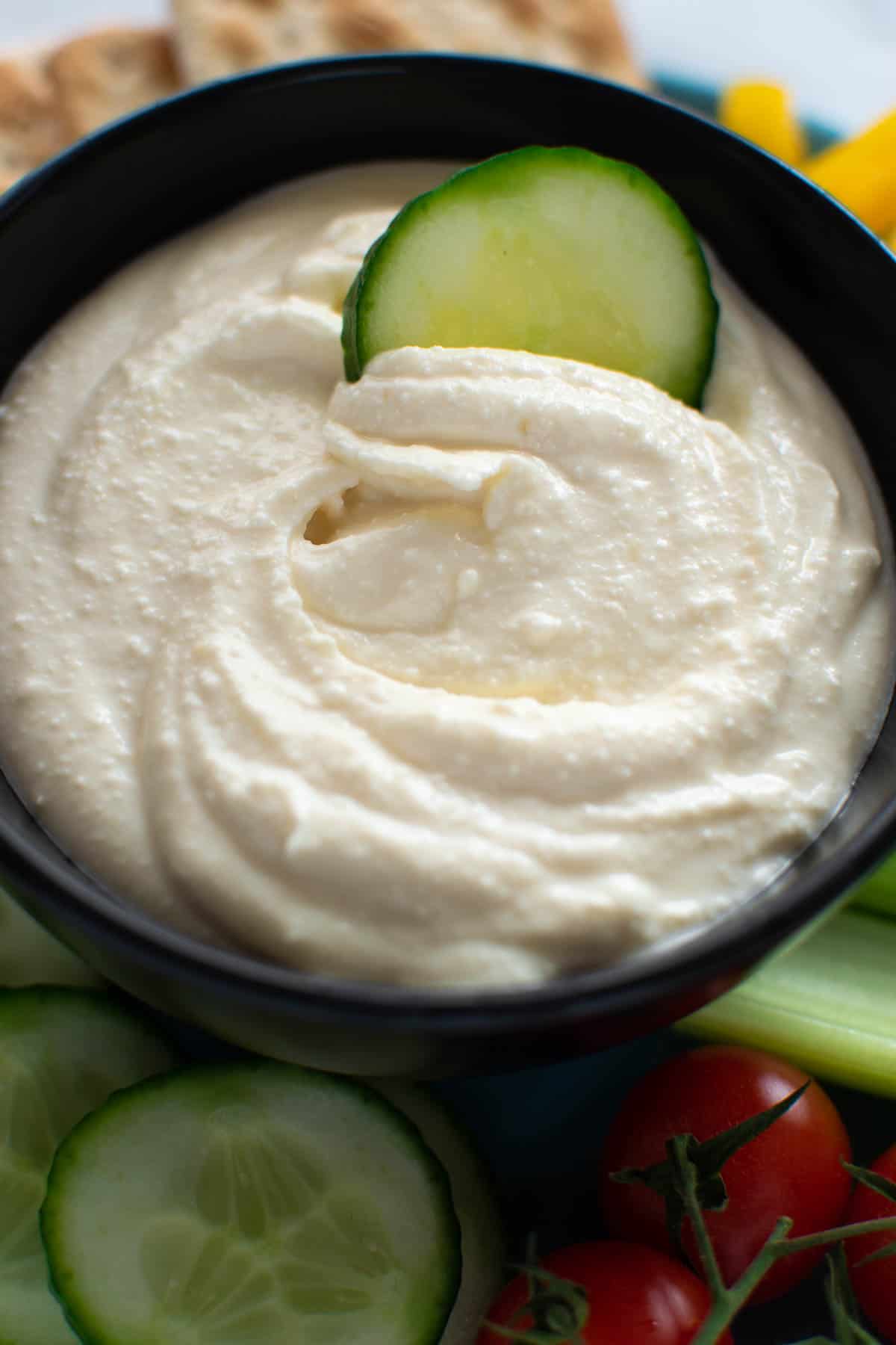 Smooth feta dip with a slice of cucumber dipped into it.