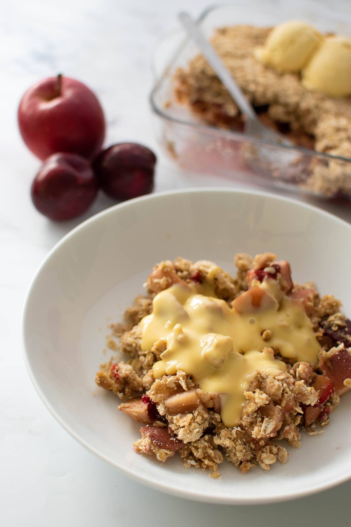 A plate with plum and apple crumble with custard.