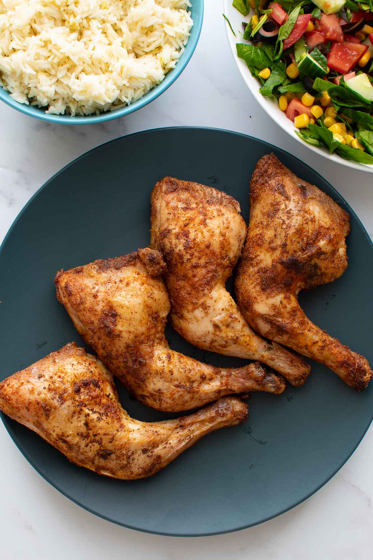 A plate of baked chicken leg quarters, with rice and salad on the side.