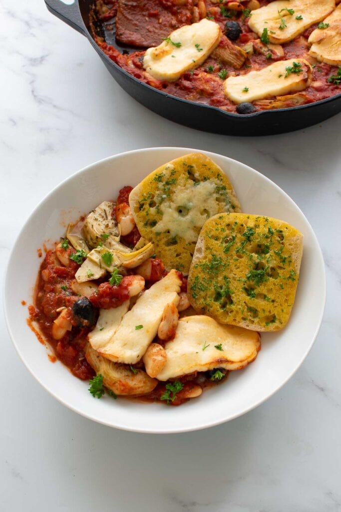 A bowl with baked halloumi, tomato sauce and garlic bread.