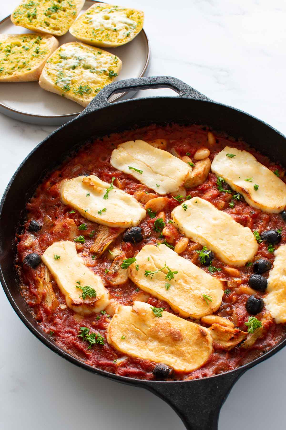 A pan with halloumi, tomato sauce, artichokes, butter beans and black olives.