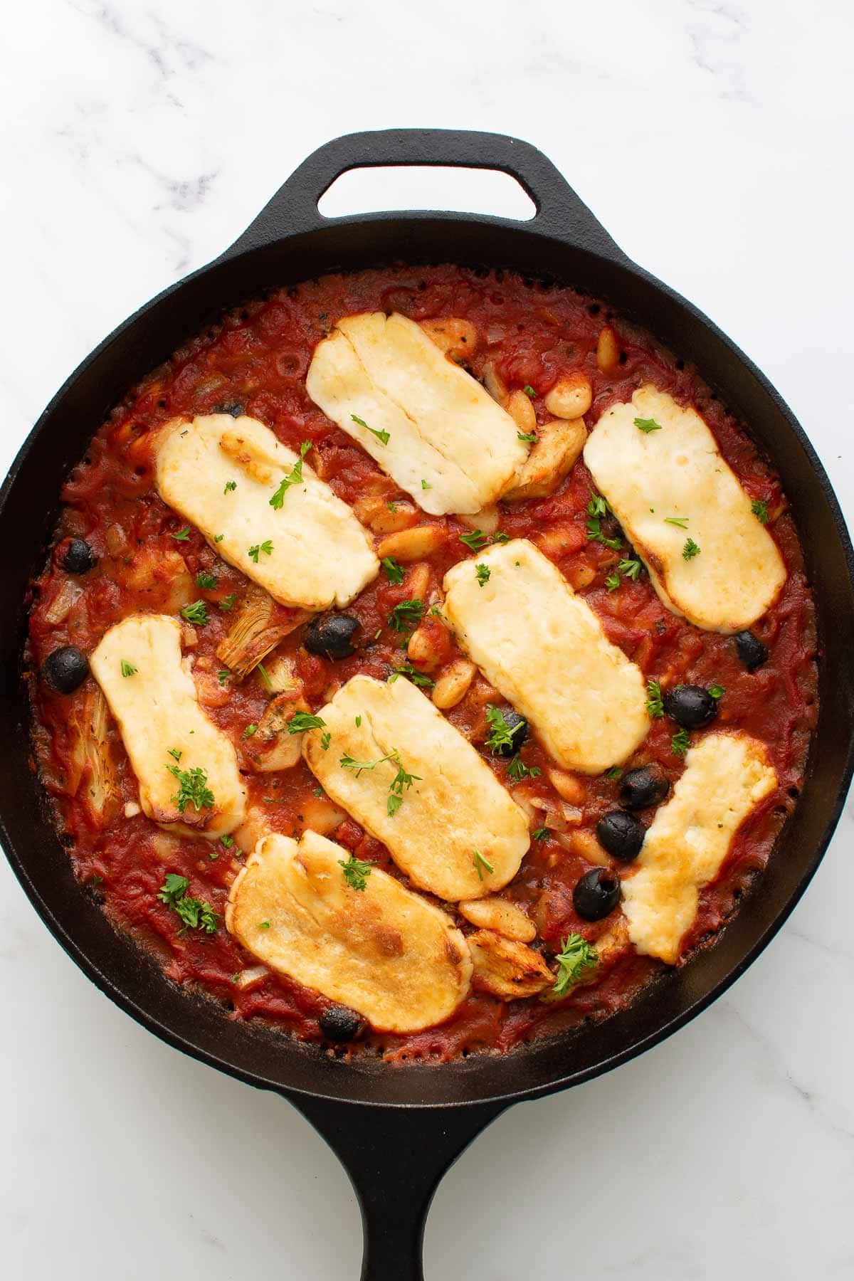 Baked halloumi in a tomato sauce with olives and beans.