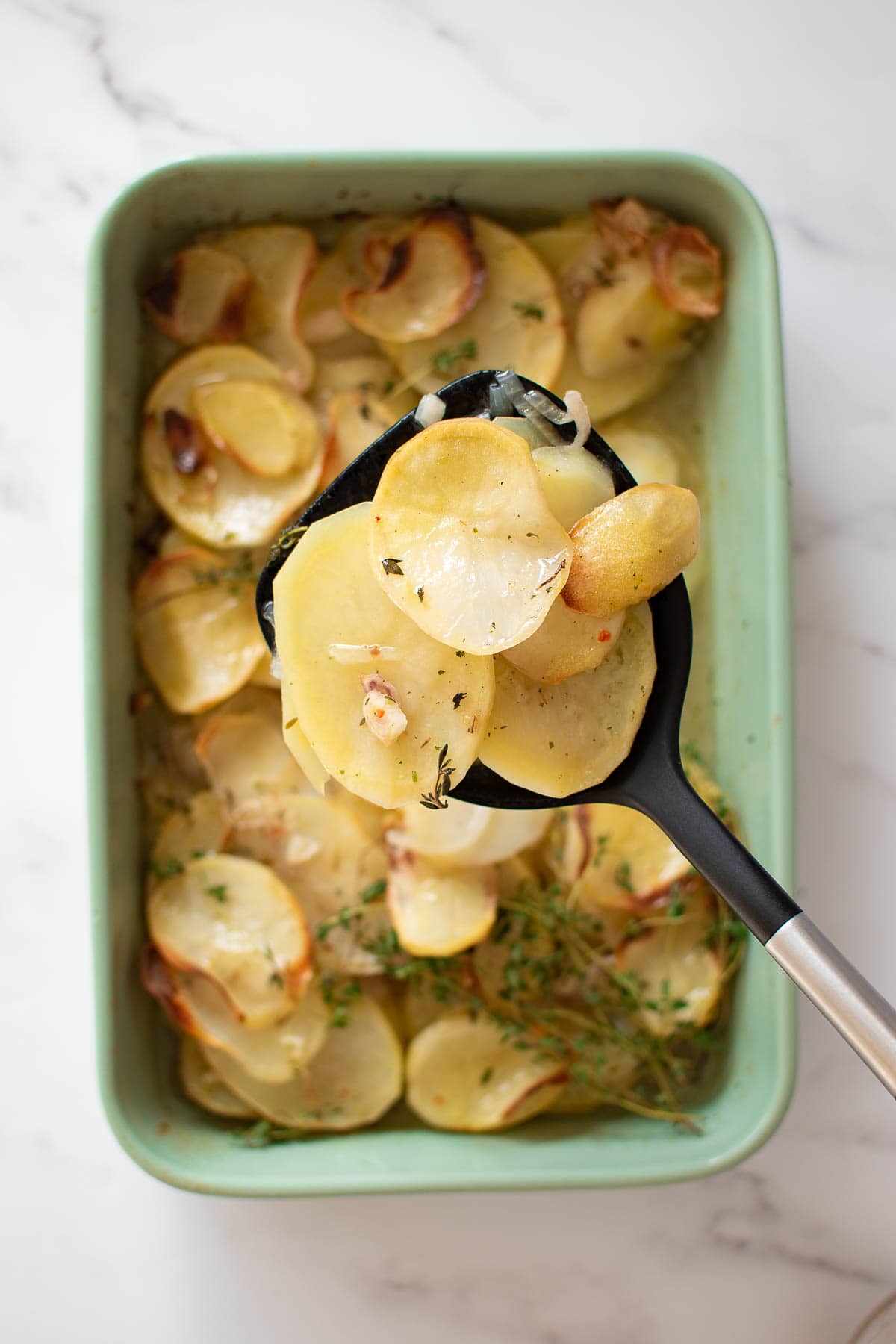 A spoon serving a potatoes of roasted sliced potatoes.