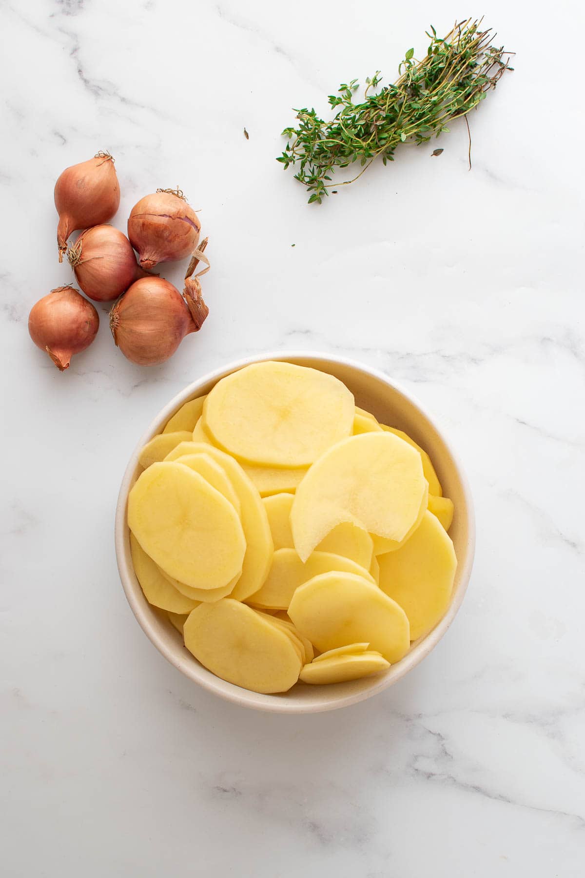 Sliced potatoes with thyme and shallots on the side.