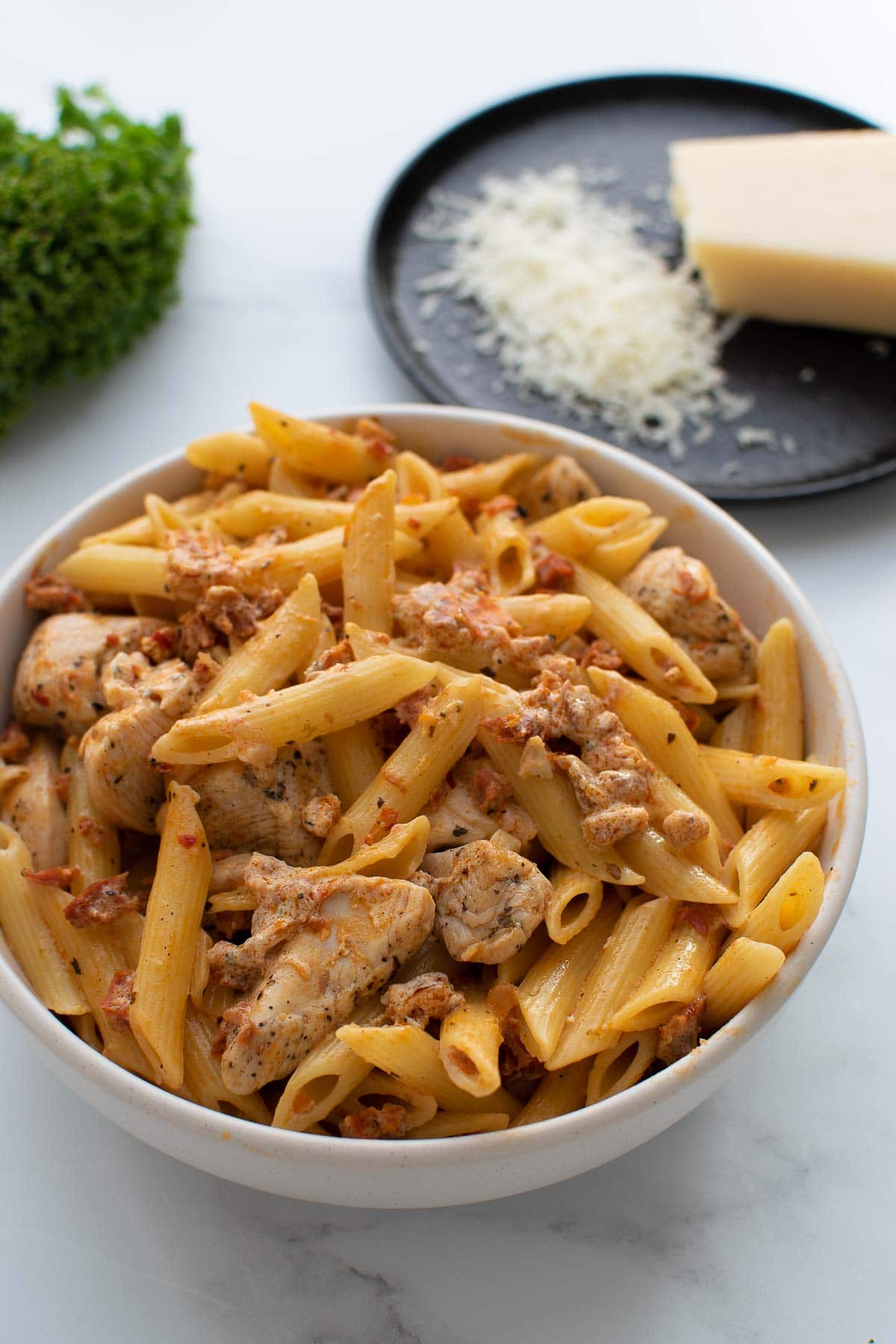 A bowl of chicken and chorizo pasta, with parmesan in the background.