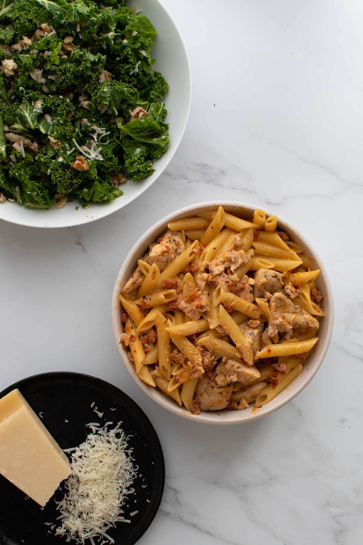 A bowl of chicken and chorizo pasta, with kale salad on the side.