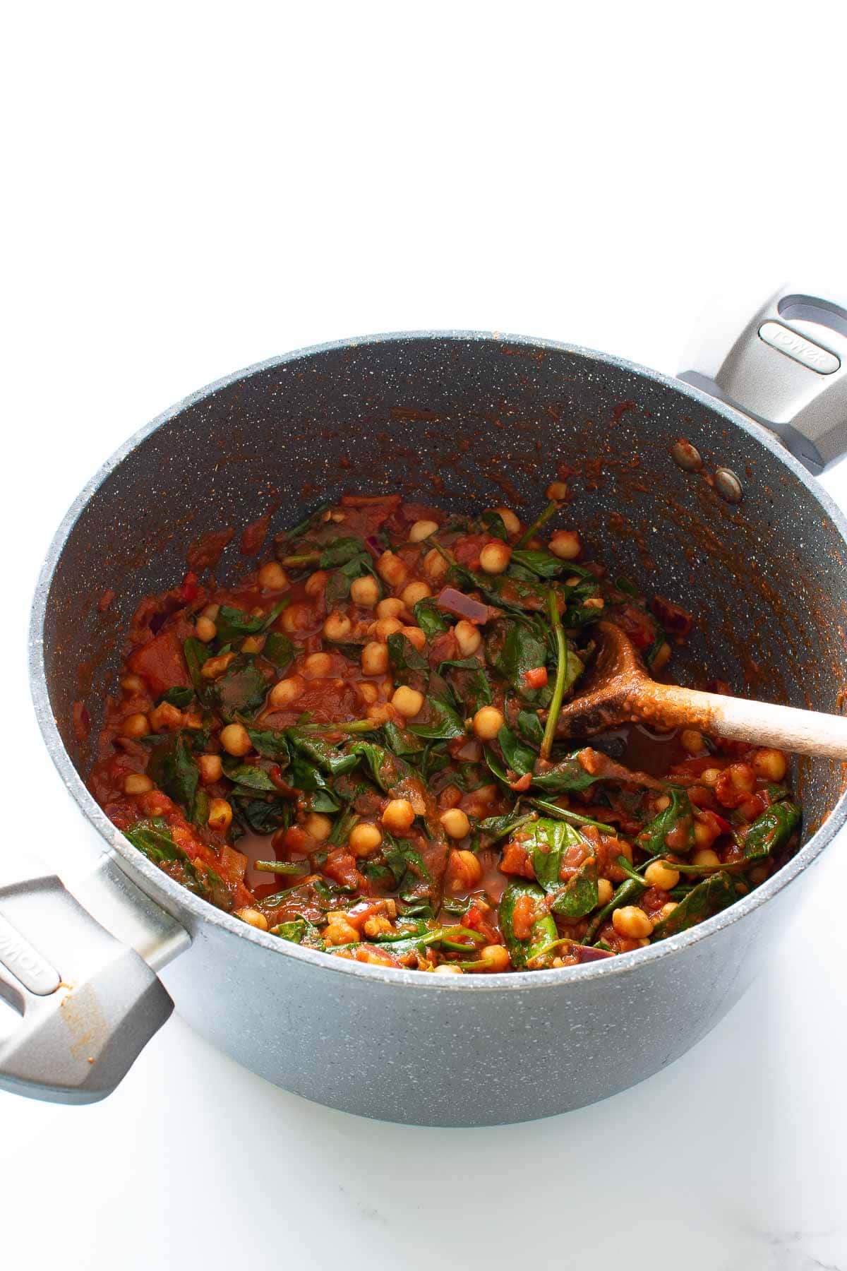 A pot of chickpea and spinach curry with tomatoes.