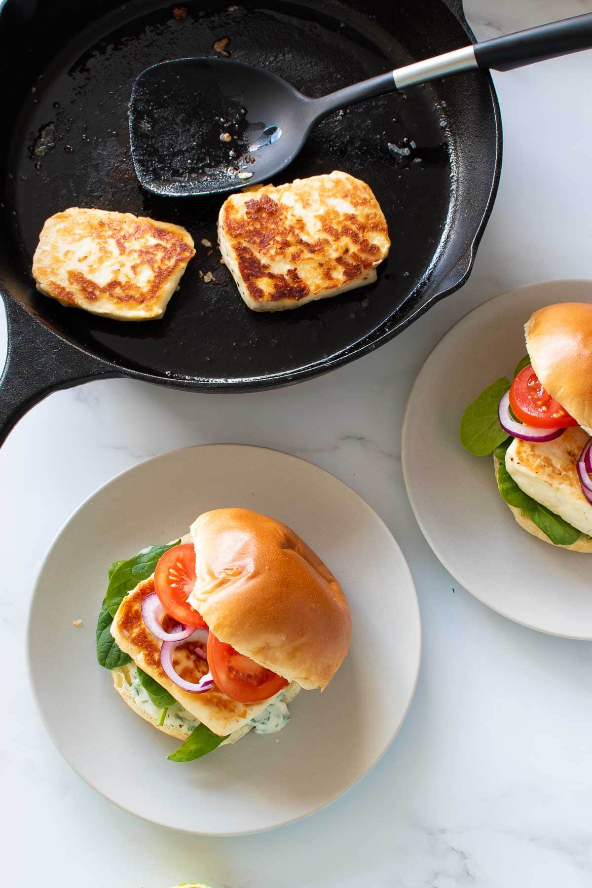 Halloumi burgers, with a pan of fried halloumi in the background.