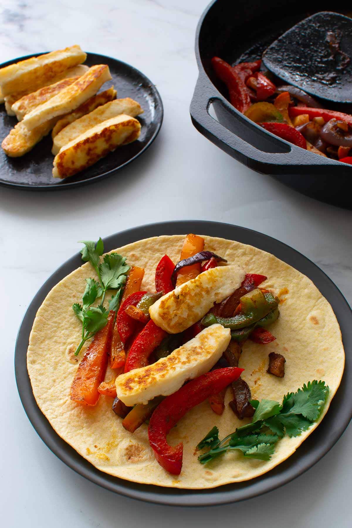 Halloumi fajita on a plate, with a pan with peppers in the background.