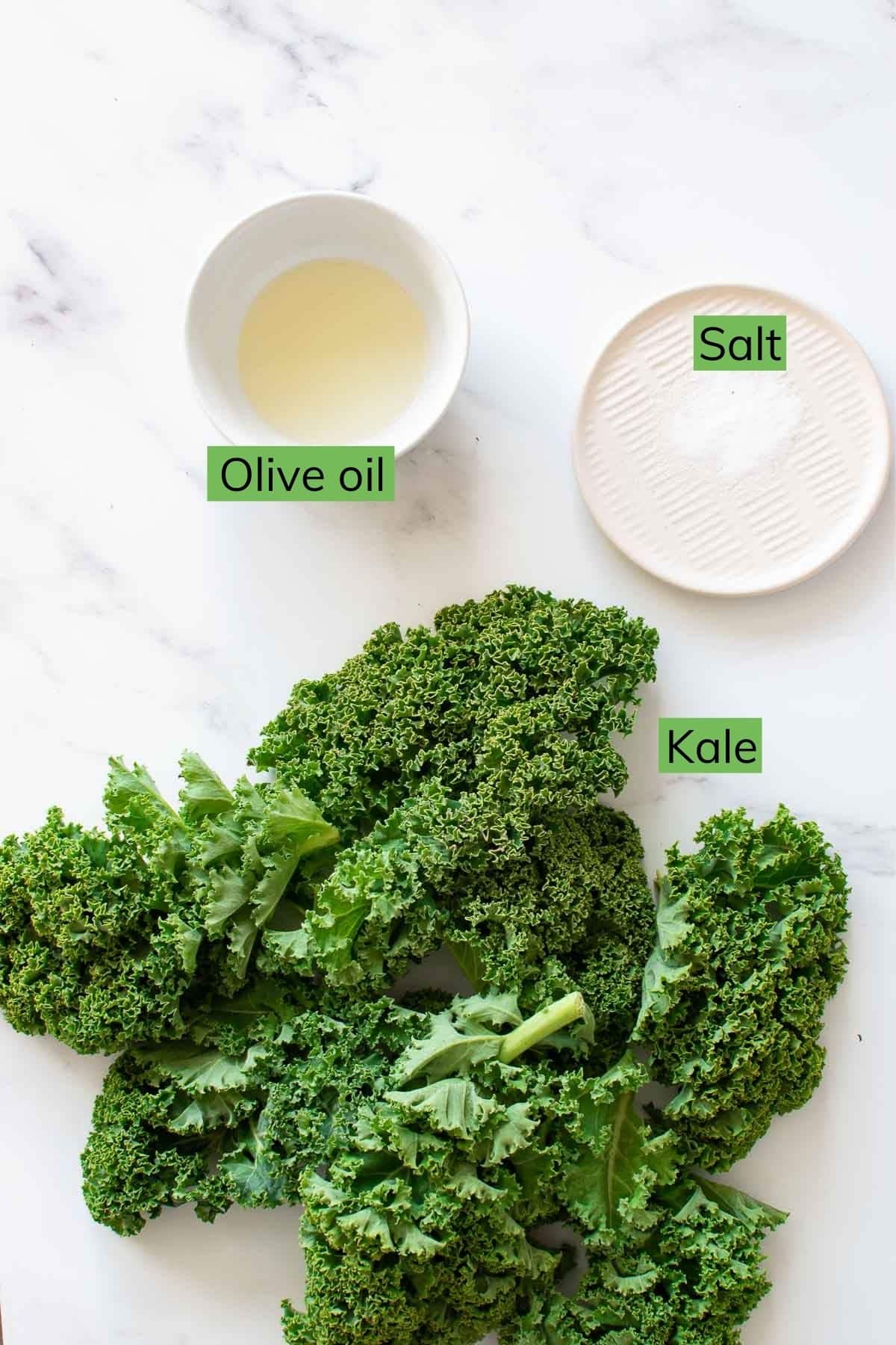 Olive oil, salt and kale on a table.