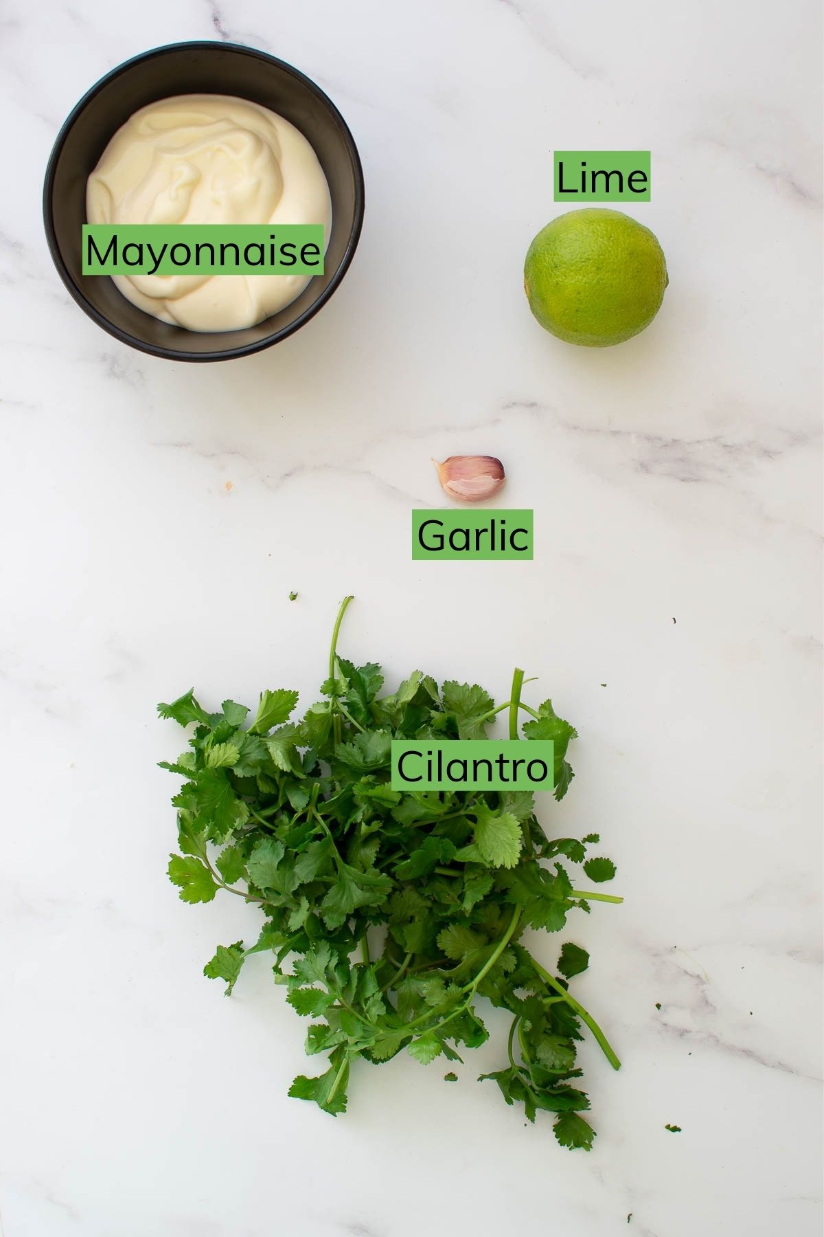 Mayonnaise, cilantro, lime and garlic laid out on a table.