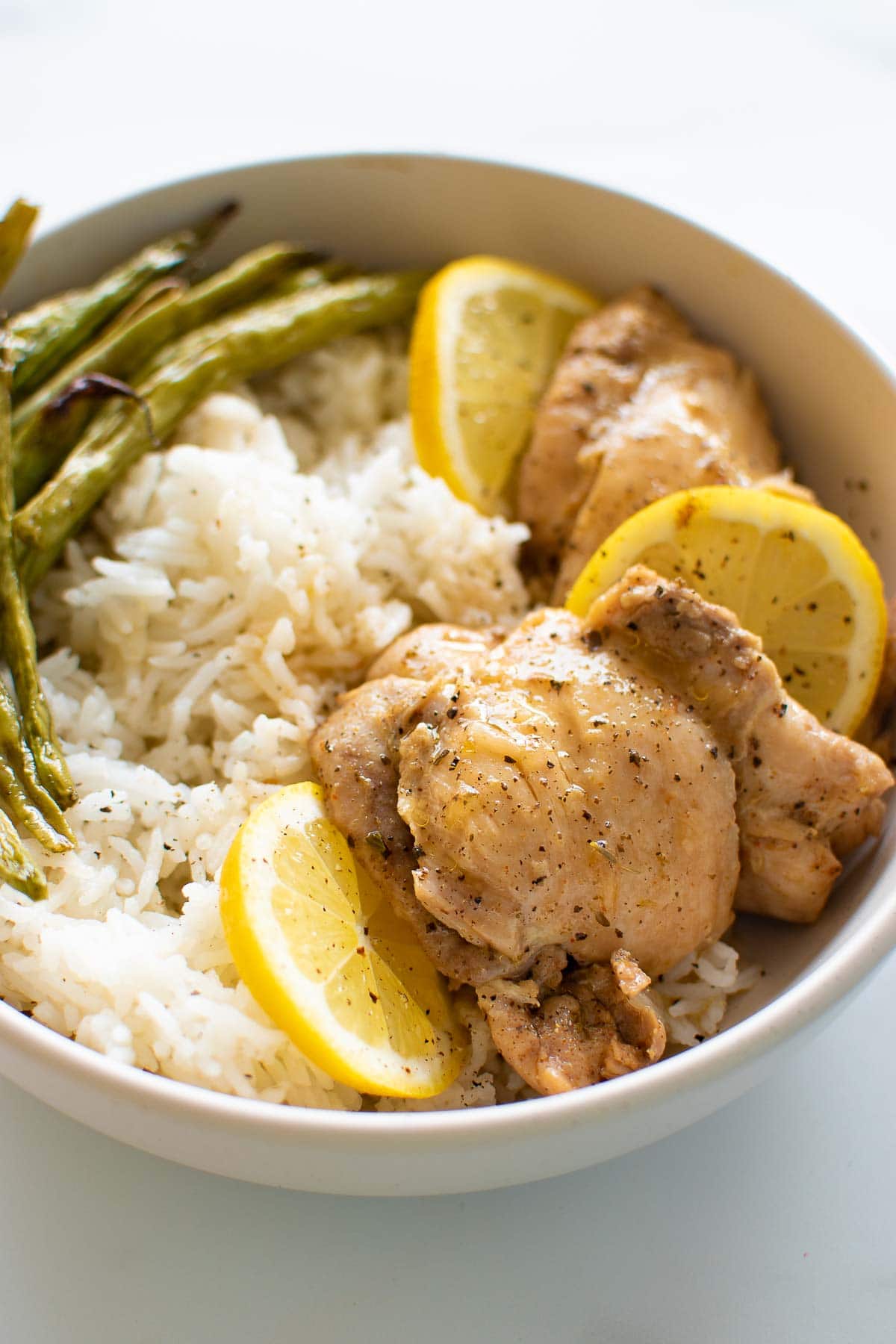 Lemon garlic chicken thighs in a bowl with rice and green beans.