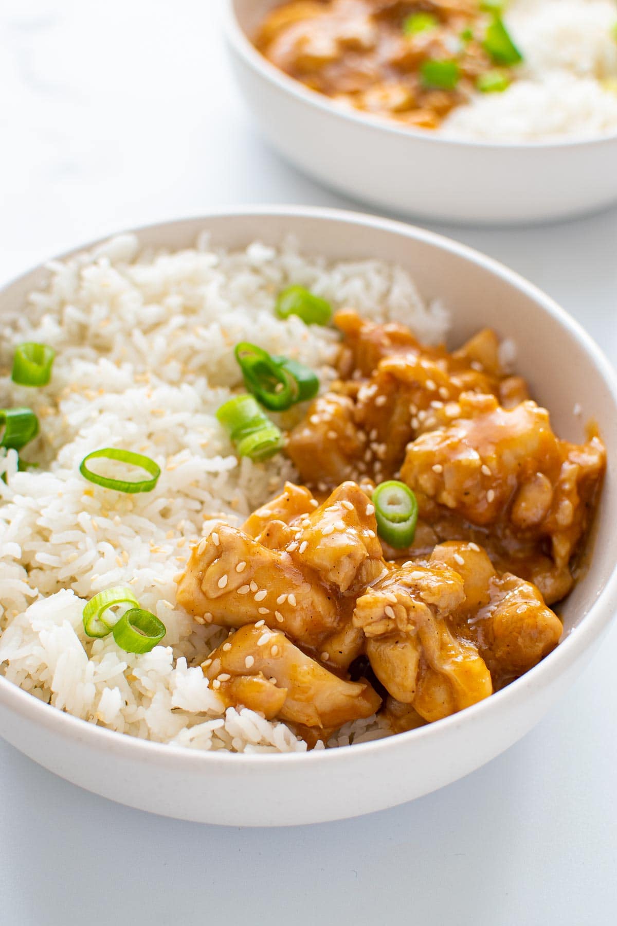 A bowl with sticky orange chicken, rice and green onions.