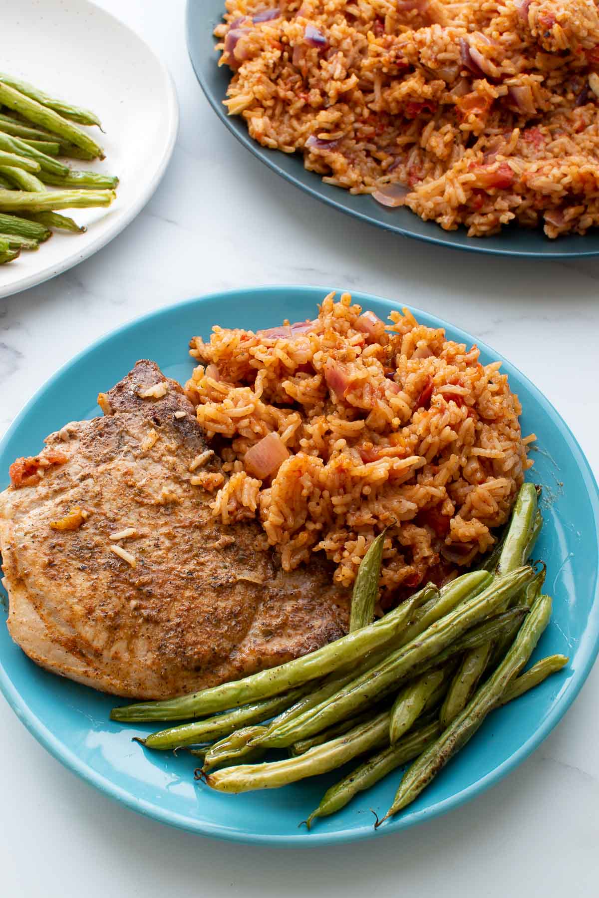 A plate with pork chop, rice and roasted green beans.