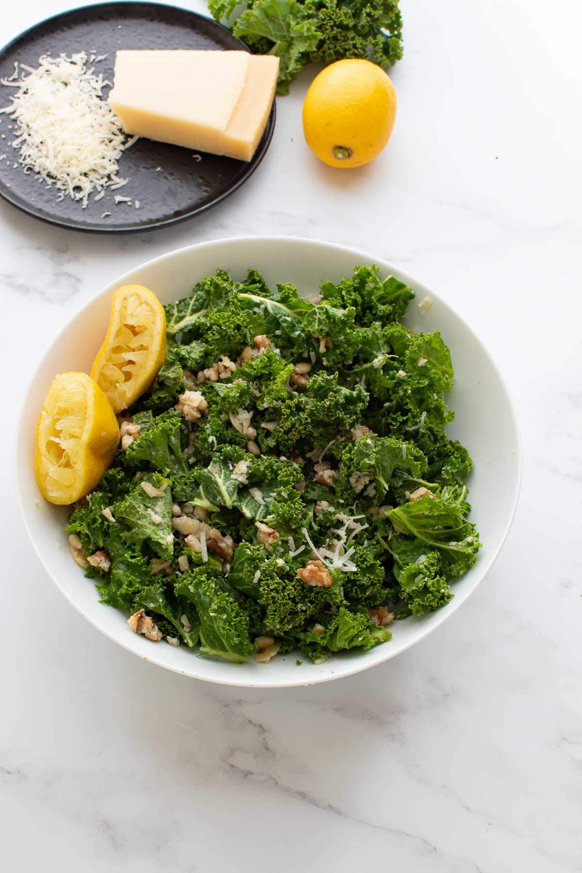 A bowl of lemon kale salad, with lemon and parmesan in the background.