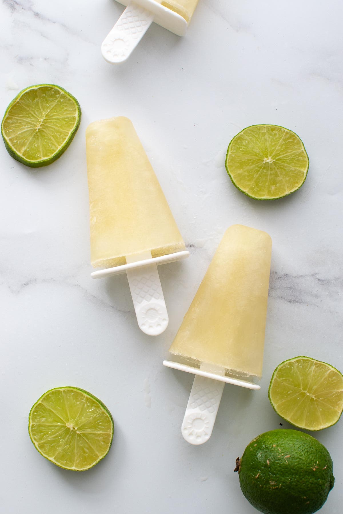 Two lime popsicles on a table with lime slices.