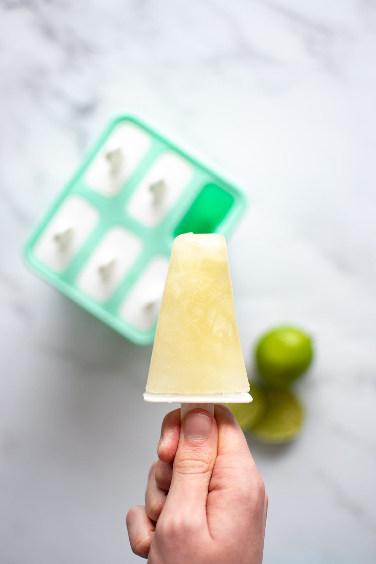 A hand holding up a popsicle above a popsicle mold.