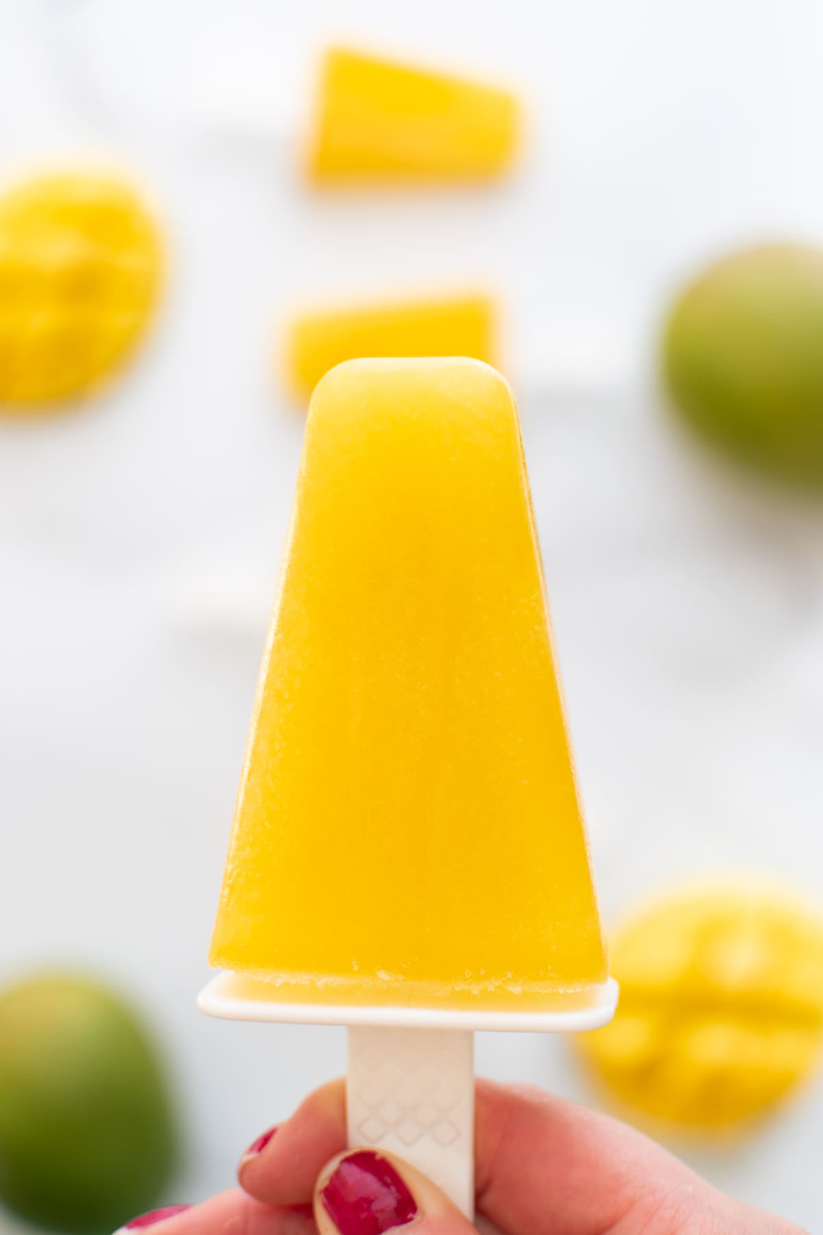 A hand holding up a yellow popsicle with mango juice.