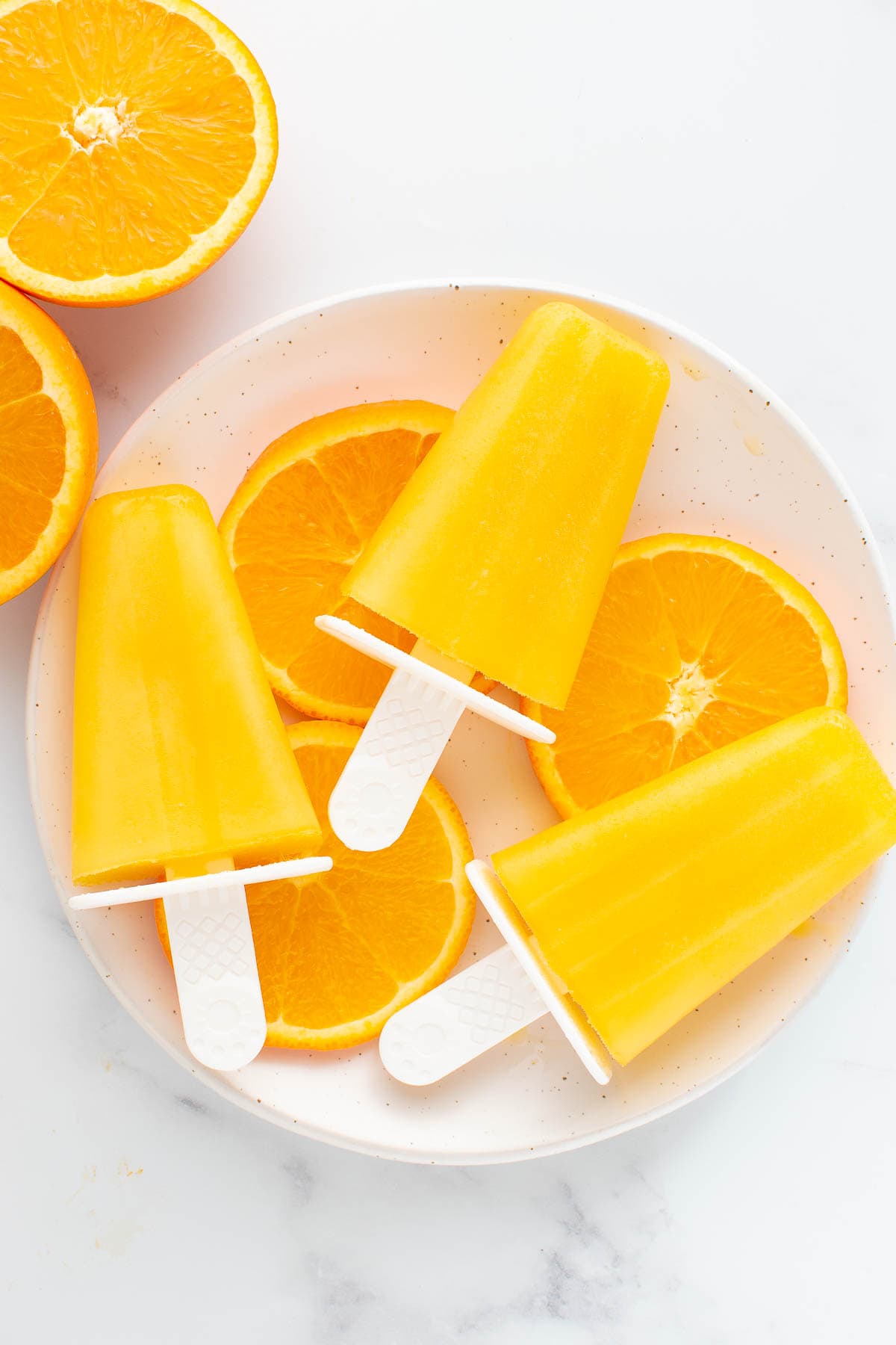 Three orange popsicles on a table.