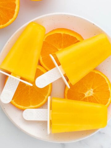 Orange popsicles laid on top of orange slices.