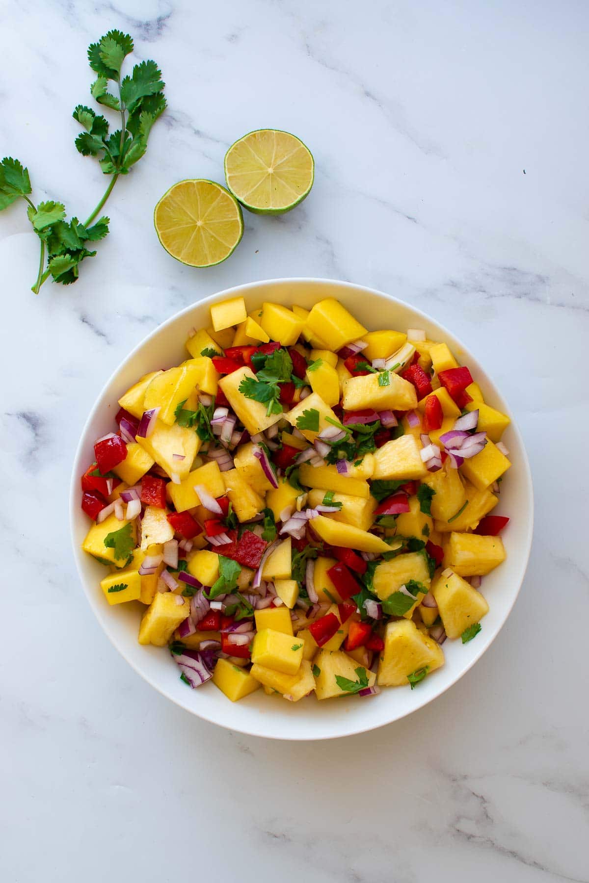 A bowl of mango pineapple salsa, with lime and cilantro on the side.