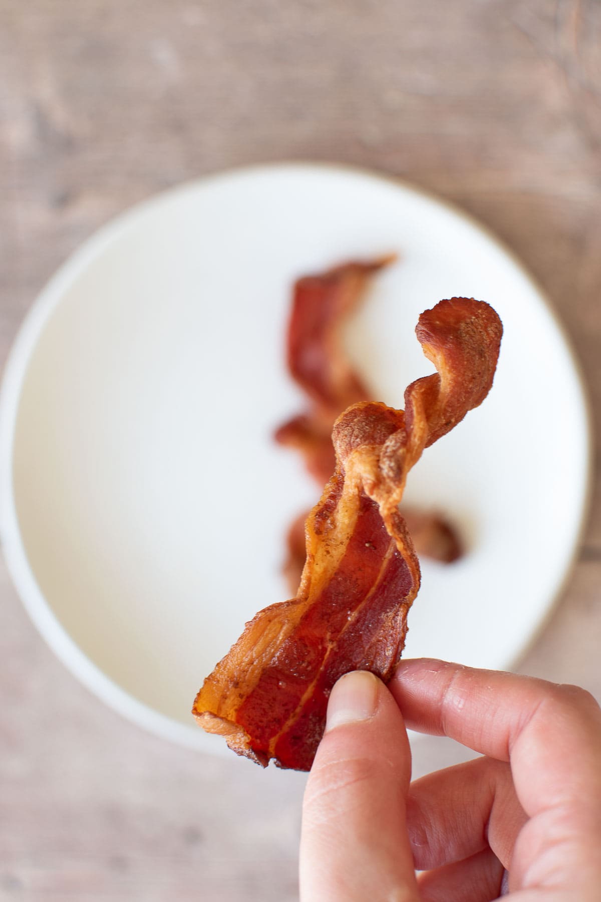 A hand holding up a crispy piece of bacon.