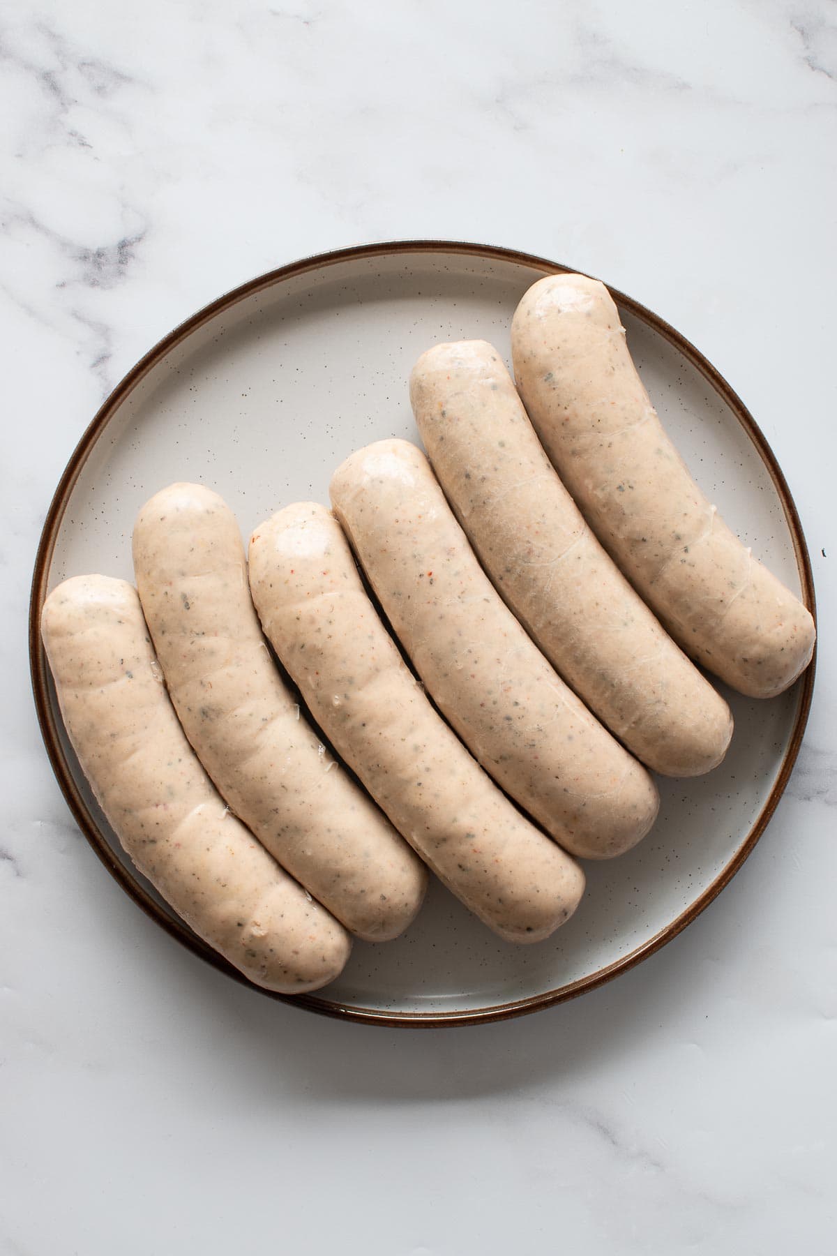 Raw bratwurst sausages on a plate.